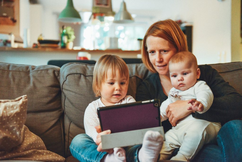 uma mãe e seus dois filhos, em casa, vendo algo em um tablet